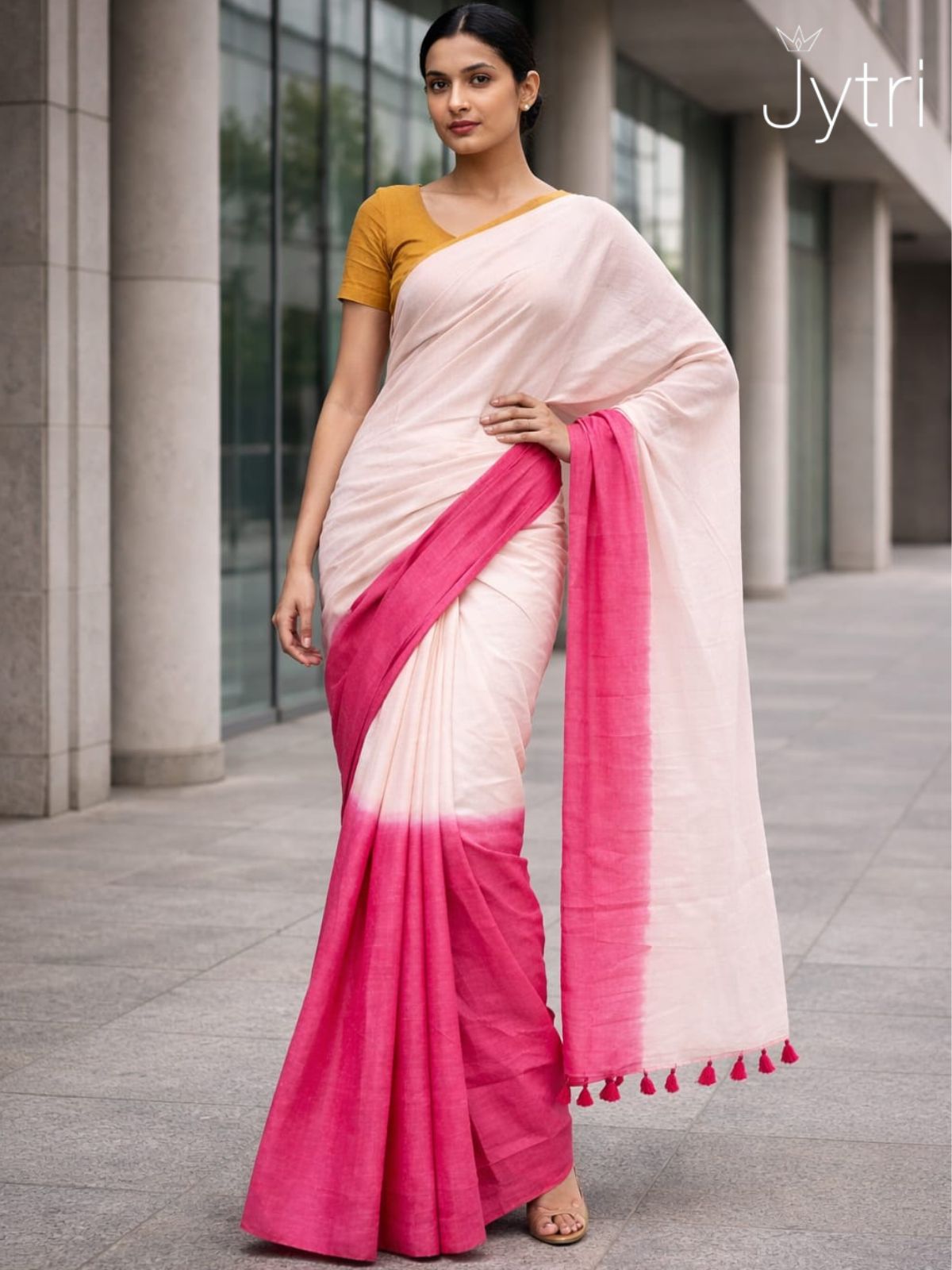 Woman wearing pink ombre cotton saree with beige base and tassel pallu in modern outdoor setting