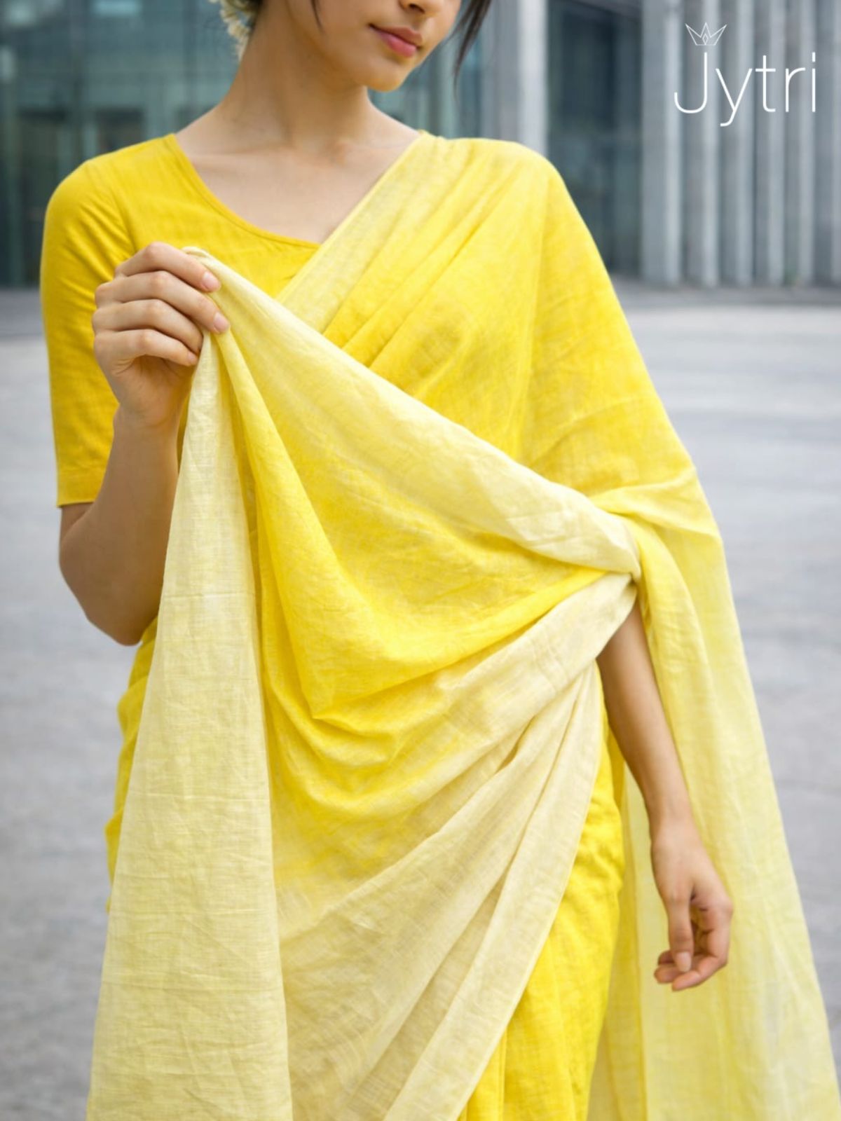 Woman wearing yellow ombre cotton saree with soft gradient and tassel pallu in modern outdoor setting